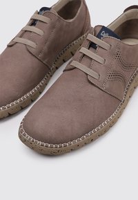 Zapatos sintéticos marrones con una textura suave, que cuentan con un diseño de cordones, detalle perforado en el lateral y una suela de goma moteada.
