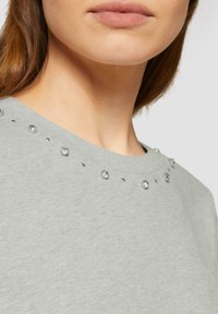 Grijze korte mouw top met een ronde halslijn versierd met ronde rhinestones en kleine studs langs de schoudernaad voor een textuur effect.