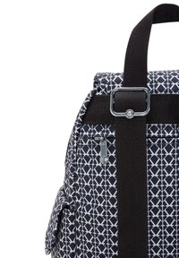 Mochila de patrón en blanco y negro con exterior de tela, bolsillo con cremallera y un asa negra resistente. Presenta un diseño geométrico y tela texturizada.