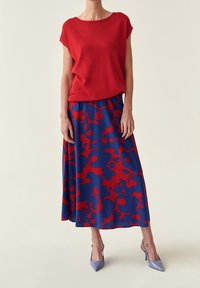 Rode top met korte mouwen en ronde hals, gecombineerd met een lange blauwe rok met een rood bloemenpatroon. Lichtpaarse hoge hakken.