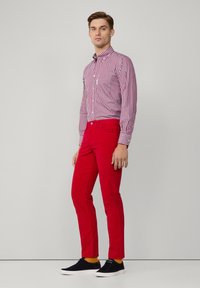 Rode strakke broek gecombineerd met een rood-wit gestreept hemd met knopen; model draagt zwarte sneakers met gele accenten.