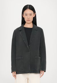Blazer in denim nero con revers, chiusura a un bottone, due tasche frontali e dettagli di cucitura a vista. Tessuto morbido, vestibilità rilassata.