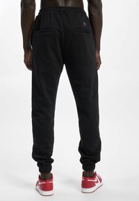 Zwarte sweatpants met een elastische tailleband en boorden, met twee achterzakken. Vergezeld van rode en witte sportschoenen. Soepele textuur.