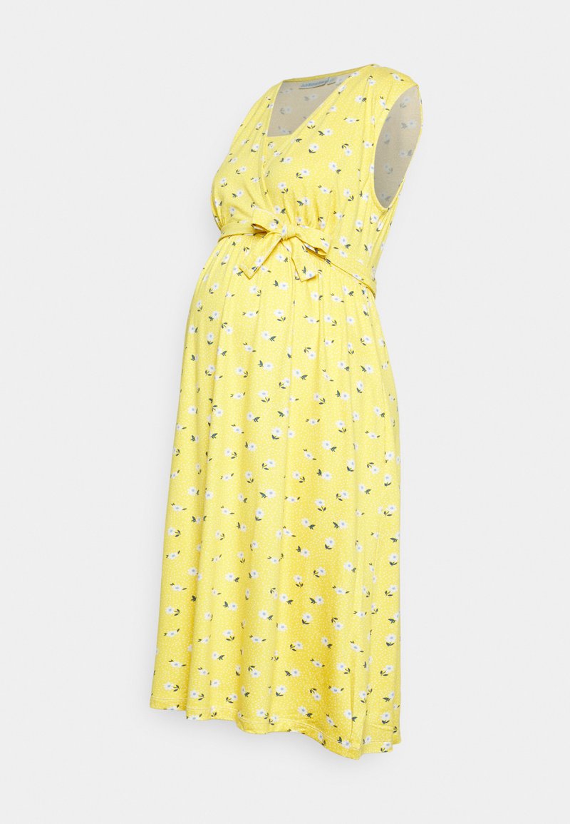 Vestido de maternidade amarelo com mangas curtas, decote em V, cintura com laço e padrão floral. Tecido leve com bolinhas e uma forma fluída.