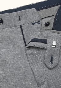 Gråt mønstret stof med en tekstureret finish, med en blå inderside og flere knapper, inklusive en lås og syningsdetaljer.