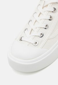 Witte canvas sneakers met een gestructureerd oppervlak, ronde neus en rubberen zool; voorzien van witte veters en metalen oogjes voor bevestiging.