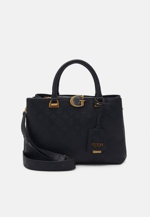 Black Guess handbag with embossed logo pattern, gold hardware, dual handles, detachable shoulder strap, and a branded tag hanging on the front.