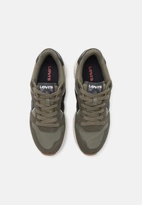 Zapatillas deportivas verdes con una mezcla de tejidos texturizados y ante, cordones redondos, acentos en negro y un logo en la lengüeta.