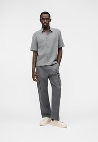 Πουκάμισο με κοντά μανίκια, γκρι καρό με κουμπιά, συνδυασμένο με γκρι παντελόνι cargo και κρεμ αθλητικά παπούτσια, με τσέπες και άνετη εφαρμογή.