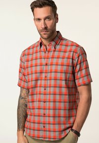 Camisa de manga corta abotonada en un patrón de cuadros rojo y gris, con cuello regular, bolsillo frontal y botones negros. La textura de la tela parece suave.