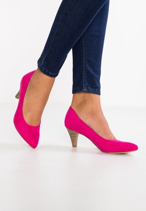 Pink suede high-heeled shoes with a pointed toe and a textured wooden heel, worn with dark blue skinny jeans.