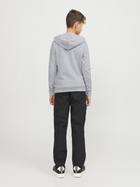 Felpa grigia con tasca a marsupio e cappuccio con cordino, abbinata a pantaloni cargo neri e sneakers nere, che mostrano un look casual.