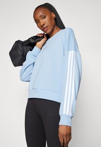 Blå sweatshirt med hvite striper på ermene, rund hals og ribbestrikkede mansjetter. Kombinert med sorte leggings og en liten svart veske.