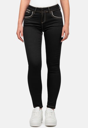 Schwarze Skinny-Jeans mit kontrastierenden gelben Nähten, Fronttaschen und einer taillierten Passform, kombiniert mit weißen Sneakers.