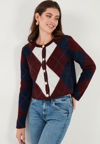 Cardigan in burgundy, navy, and cream featuring a diamond pattern, round neckline, and gold buttons. Long sleeves with relaxed fit.