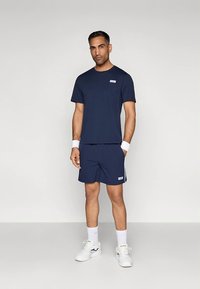 Marineblå sportset bestående av en kortärmad tröja och shorts. Tyget är slätt; shortsen har en sidodetalj. Setet inkluderar vita sportskor och handledsband.