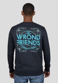Mörkblå sweatshirt med en stor turkos grafisk design på baksidan, som visar texten "The WRONG FRIENDS Design House."
