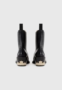 Bottines en cuir noir avec des zips sur les côtés et des panneaux élastiques ; elles présentent un talon festonné de couleur crème distinct.