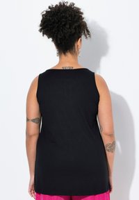 Czarny bezrękawnik z okrągłym dekoltem, wykonany z gładkiego materiału. Posiada luźny krój, noszony z różowymi spodniami o fakturze.