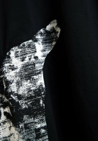 Acercamiento de tela negra con un patrón texturizado abstracto en blanco y negro cosido en el material.