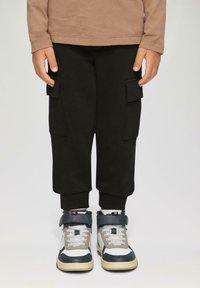 Schwarze Cargo-Hosen mit seitlichen Taschen, gerippten Bündchen, kombiniert mit grauen und marineblauen High-Top-Sneakern mit weißen Akzenten und einer strukturierten Sohle.