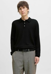 Juodas ilgos rankovės polos marškinėliai su apykakle, turintys tris mygtukus ir lygų paviršių, derinami su pilkais kostiumo kelnėmis ir juodu diržu.