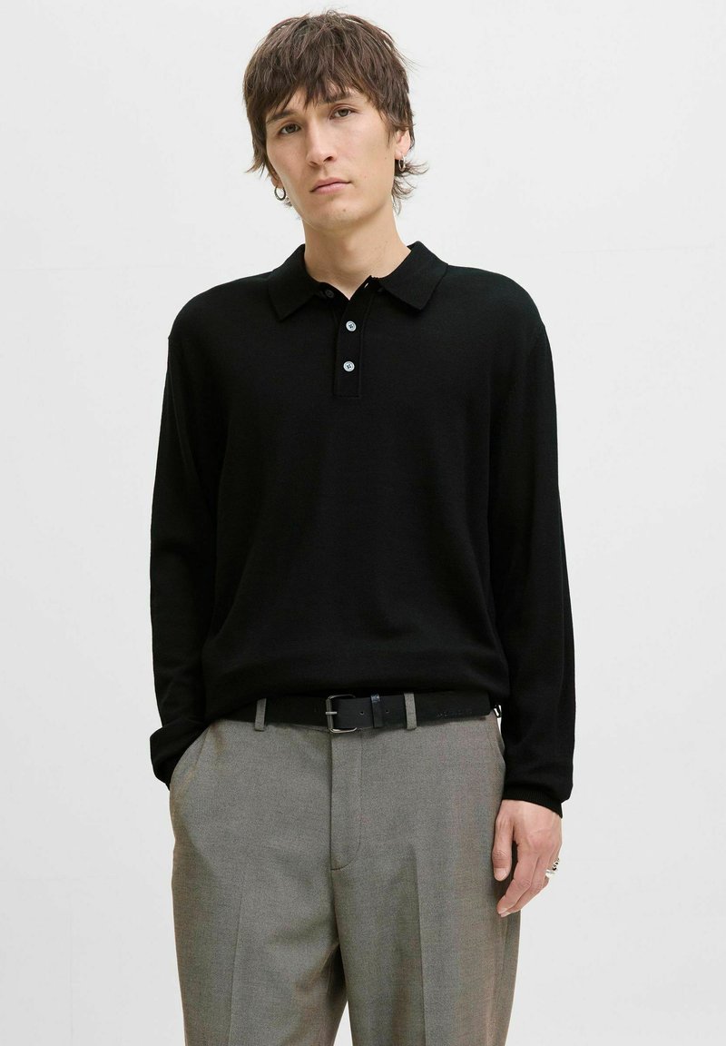 Juodas ilgos rankovės polos marškinėliai su apykakle, turintys tris mygtukus ir lygų paviršių, derinami su pilkais kostiumo kelnėmis ir juodu diržu.