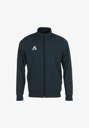 Veste zippée bleu marine en tissu doux, avec un col haut, des manches longues et un logo blanc sur la poitrine gauche.