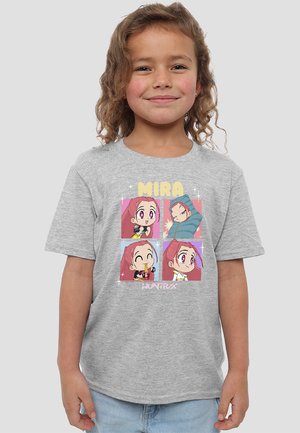 Mädchen mit lockigem Haar lächelt, trägt ein graues T-Shirt mit vier bunten Cartoon-Charakterzeichnungen und dem Text "MIRA" und "HUNTRAX".