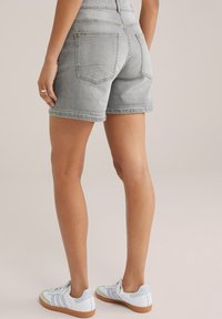 Pelēka denim augstuma šorti ar plīsušo apmalīti, ar divām aizmugurējām kabatām, kopā ar baltiem čības ar krāsainiem akcentiem.