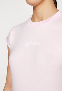 T-shirt de algodão rosa claro com mangas curtas e gola redonda. Apresenta o logótipo branco "adidas" impresso no peito.