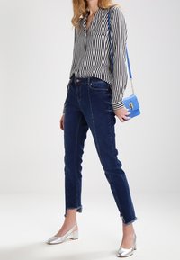 Camiseta de manga larga a rayas en blanco y negro, vaqueros azules con dobladillo deshilachado, zapatos plateados de tacón grueso y un bolso pequeño azul.