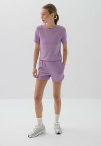 Jasnofioletowy zestaw odzieży sportowej składający się z koszulki z krótkim rękawem i szortów, wykonany z miękkiego, lekkiego materiału z elastycznym pasem i kieszeniami.