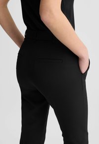 Zwarte op maat gemaakte broek met een slim fit, voorzien van zijzakken en een gladde textuur. De achterkant heeft een nette afwerking zonder zichtbare naden.