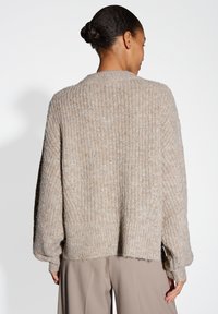 Beige knitted sweater with a loose fit, ribbed texture, and dropped shoulders. Features a wide neckline and ribbed cuffs, providing a relaxed look.