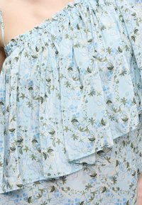 Φόρεμα ανοιχτού χρώματος μπλε, χωρίς τιράντες, με βολάν στο ντεκολτέ και λουλουδάτο και γεωμετρικό μοτίβο σε αποχρώσεις πράσινου και μπλε.