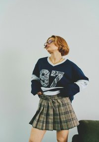 Maglione navy oversize con accenti bianchi, decorato con il numero "97" a motivo pizzo; abbinato a una gonna a pieghe in tonalità marrone e nera.