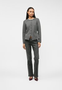 Veste grise à boutons avec des manches longues, deux poches avant et un design peplum. Assortie à un jean foncé et des talons bordeaux.