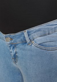 Jeans de ganga azul claro com um design clássico de cinco bolsos, apresentando um fecho de botão metálico e costura contrastante ao longo das costuras.