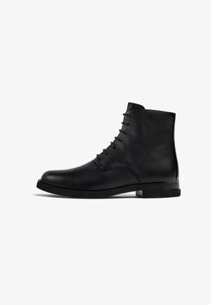 Bottine en cuir noire avec un bout arrondi et un laçage à l'avant. Elle présente une texture lisse et un petit talon carré.