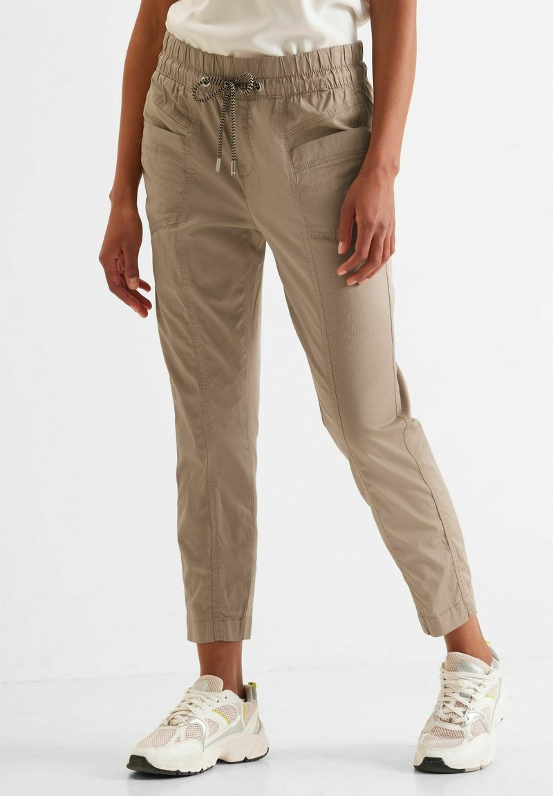 Pantalones cargo beige con cintura elástica y cordón ajustable, que presentan bolsillos laterales y un diseño de pierna ajustada.