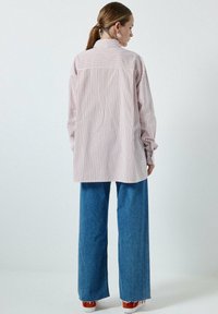 Camicia a righe bianca con strisce rosse e blu, vestibilità over, maniche lunghe e retro uniforme. Abbinata a jeans a gamba larga blu e sneakers.