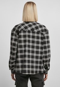 Svart og hvit rutete flanellskjorte med lange ermer, rett snitt og knappede mansjetter, med en yoke-detalj på baksiden.