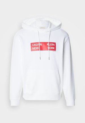 Felpa bianca con tasca frontale, caratterizzata da una stampa grafica rossa che recita "CALVIN KLEIN NEW YORK" in una tipografia audace. Coulisse regolabile.