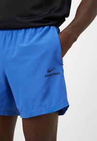 Nike Pro mænds shorts i lys blå med et sort logo på venstre lår. Letvægtsstof, elastisk talje og sidelommer.