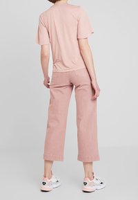 Jasnoróżowa koszulka z krótkim rękawem, zestawiona z jasnoróżowymi spodniami o szerokich nogawkach. Białe trampki z różowymi akcentami. Jednolite tło.