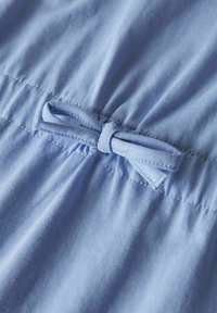 Jasnoniebieska tkanina o gładkiej strukturze, z marszczonym pasem i kokardką na środku. Miękki bawełniany materiał.