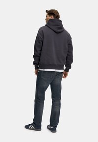 Mörkgrå kort hoodie med en stor huva, ribbade manschetter och nederkant, i kombination med blå denimjeans och marinblå sneakers med vita ränder.