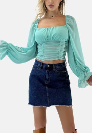 Hellgrüne, transparente Bluse mit aufgepufften Ärmeln und gerafften Details. Kombiniert mit einem dunkelblauen Jeans-Minirock mit ausgefranstem Saum.