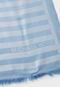 Écharpe bleu clair avec des motifs alternant entre unis et rayés, aux bords frangés et avec le logo "MICHAEL KORS" tissé dans le design.